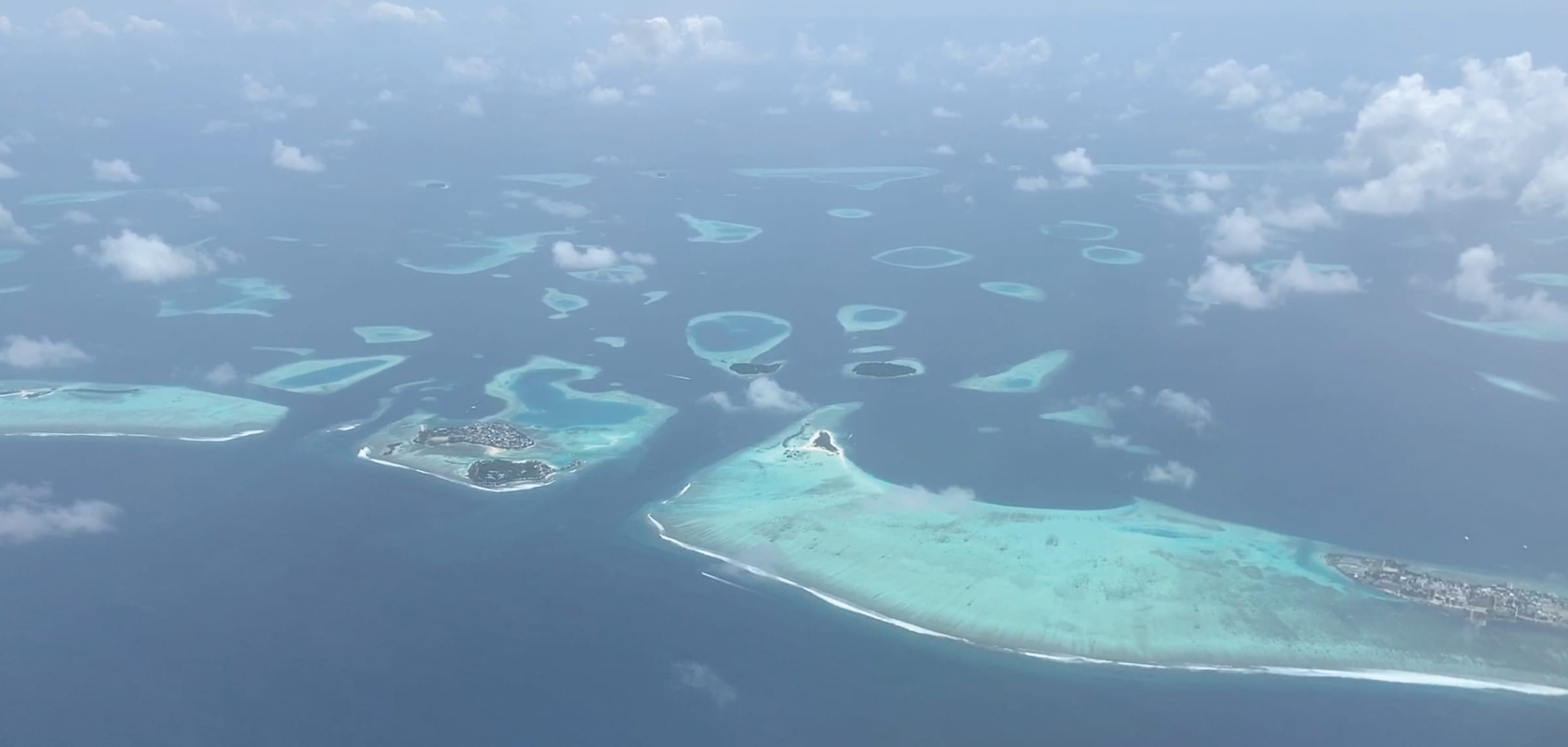 Aerial view of coral atolls and turquoise reef flats scattered across deep ocean in the Maldives.